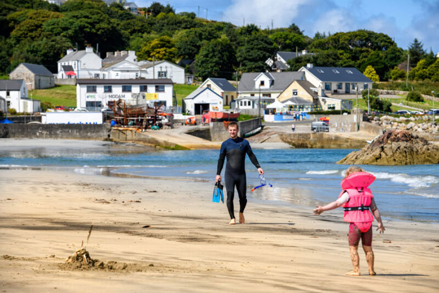 Man met snorkel in wetsuit op het strand van Arranmore Island.