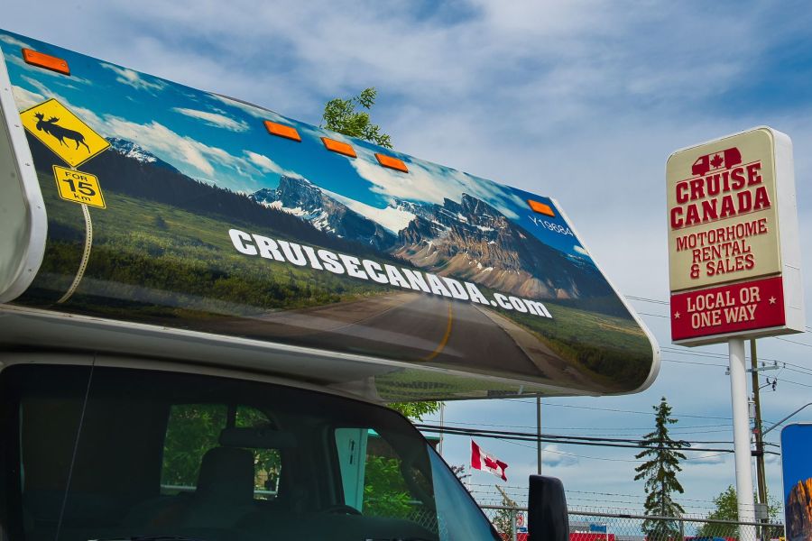Camper van Cruise Canada naast een bord van de huur locatie van Cruise Canada.