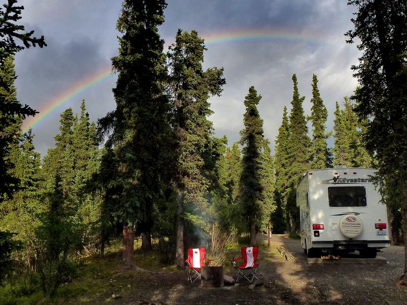 Camper van Fraserway in het bos van Canada met een regenboog op de achtergrond.