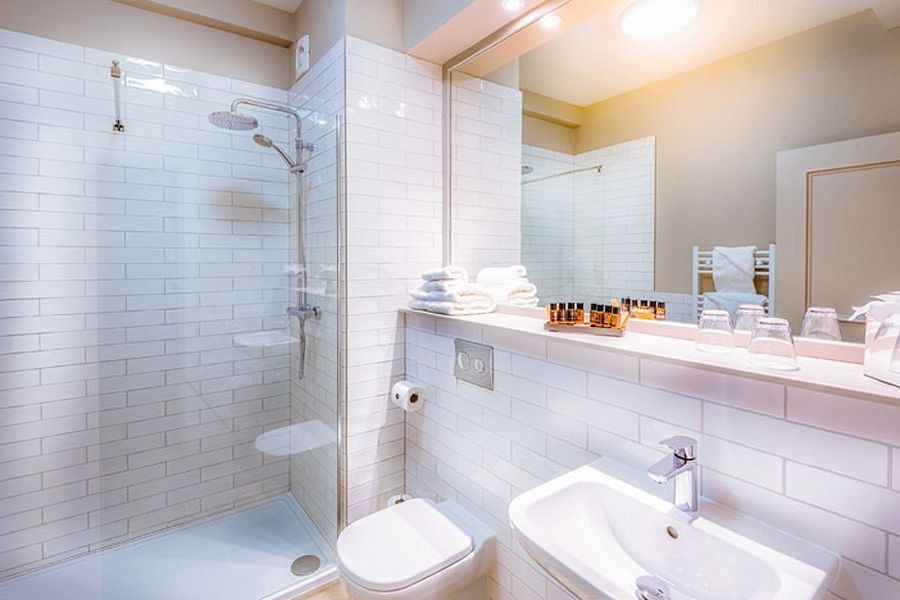Een badkamer met witte tegels en uitzicht op de wastafel, wc en douche in het Bishop`s Gate Hotel in Derry