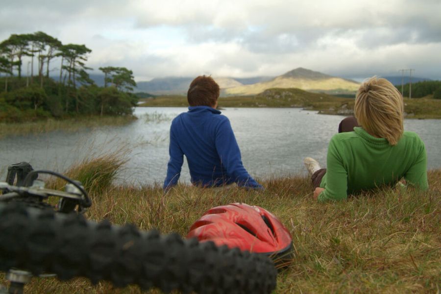 Twee fietsers rusten uit bij een meertje met uitzicht op de berg