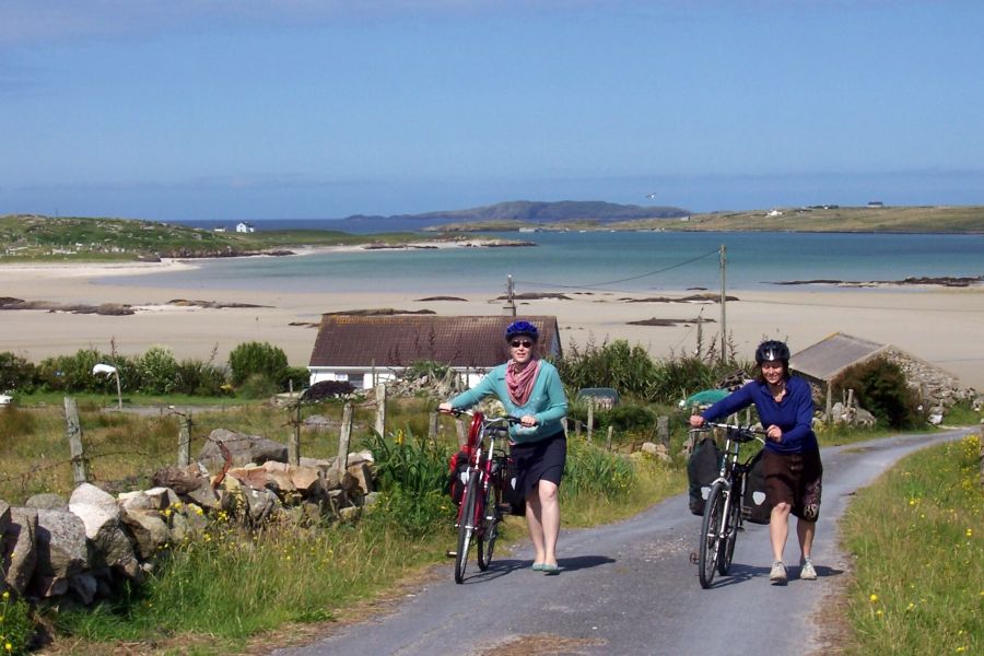 Twee fietsers met de fiets aan de hand die een heuvel omhoog lopen vanaf het strand