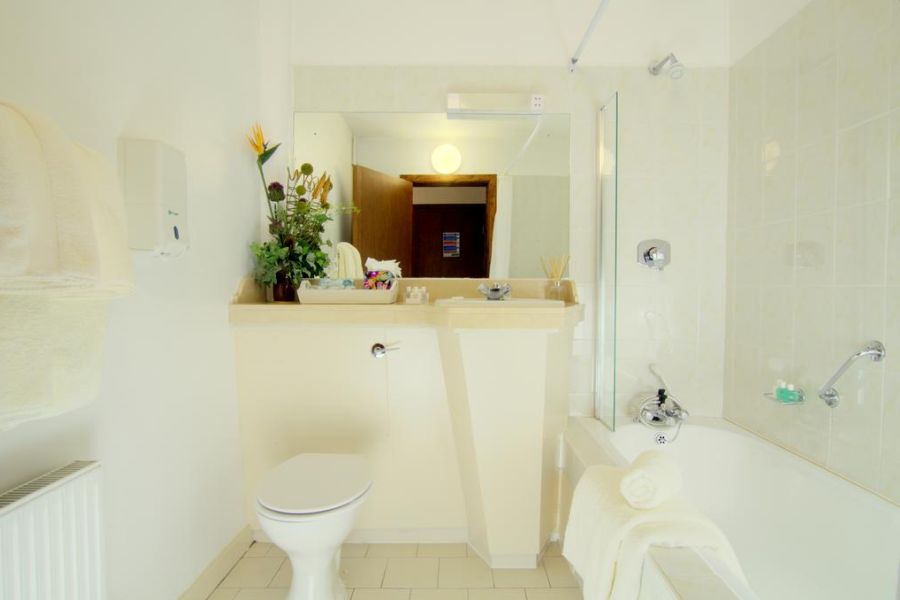 Een witte schone badkamer in het Ardagh Hotel Clifden met een toilet, een douche in bad en een grote spiegel