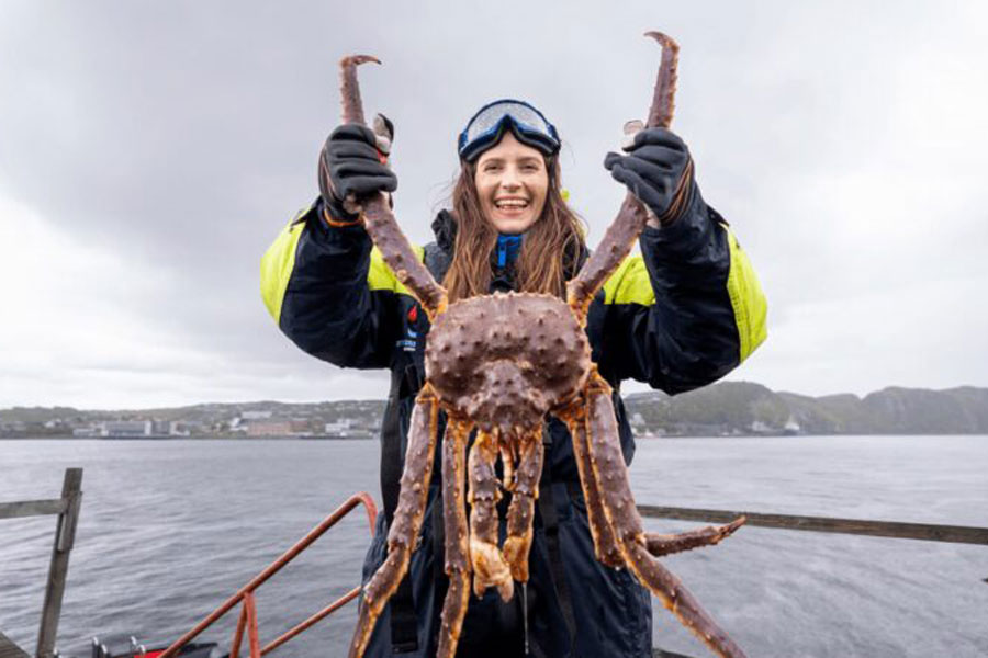 Vrouw houdt een king crab omhoog tijdens een King Crab Safari excursie in Noorwegen