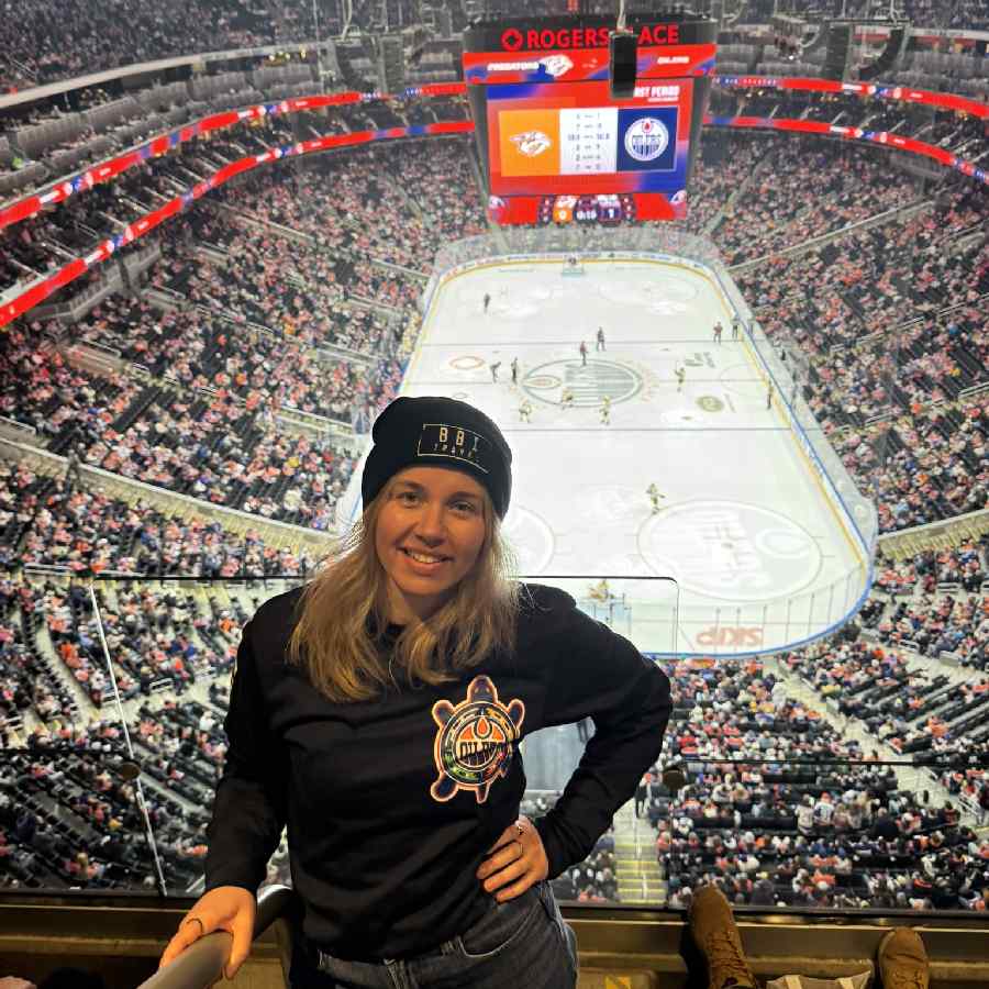 vrouw poseert voor een vol stadion tijdens een ijshockey wedstrijd van de Edmonton Oilers