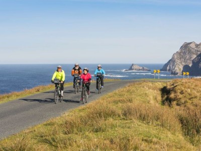 Vier fietsers met gekleurde jassen aan fietsend langs de kust van Donegal